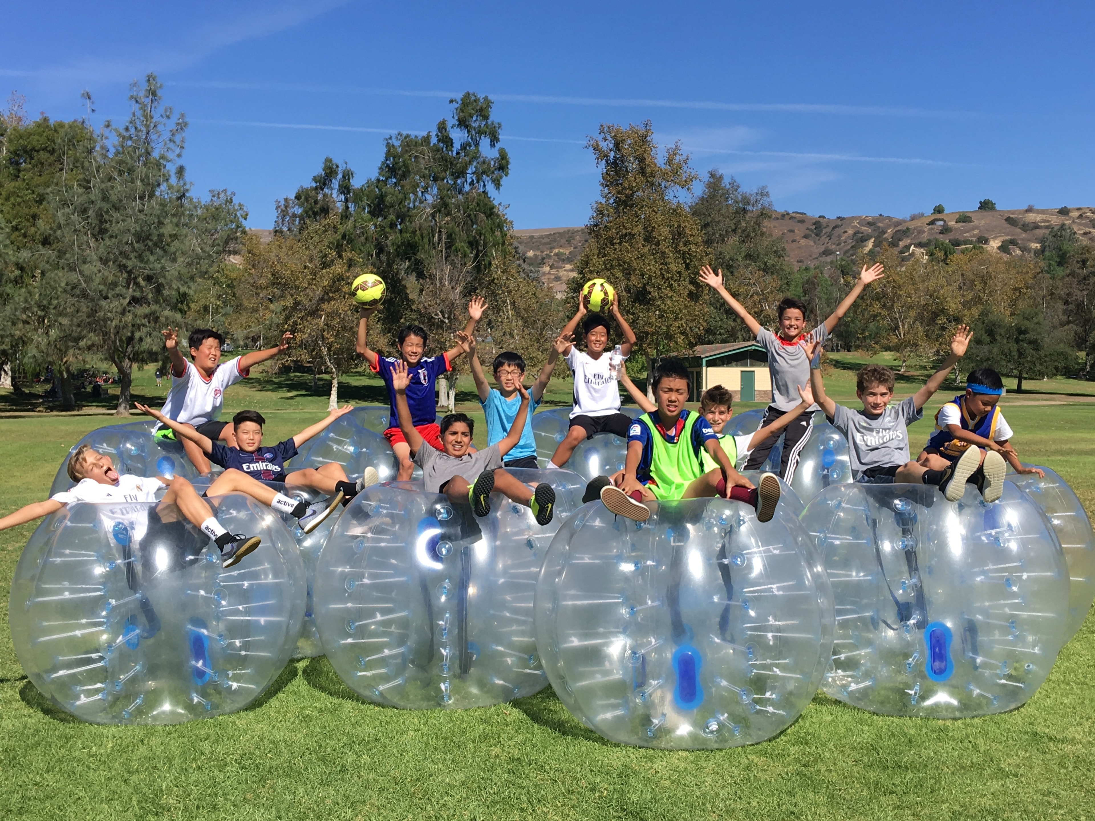 Kids in bubble suits lying on grass laughing at LA Bubble Soccer event