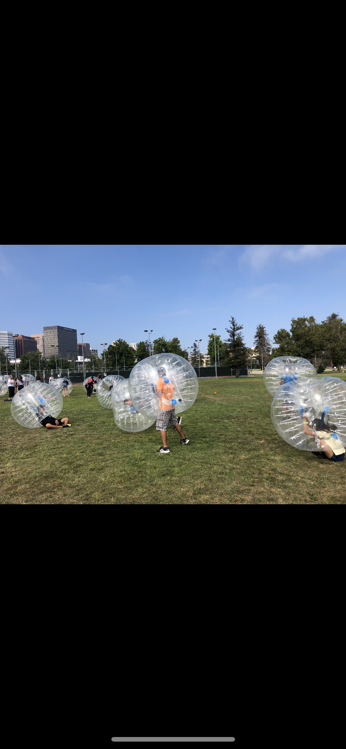 Players in bubble suits on grass field with city skyline in background