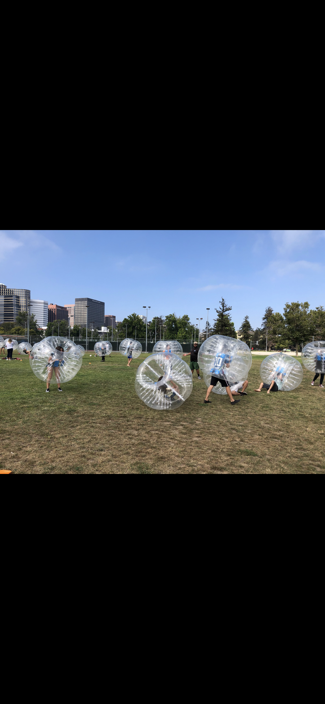Bubble soccer players colliding on grass field with city skyline